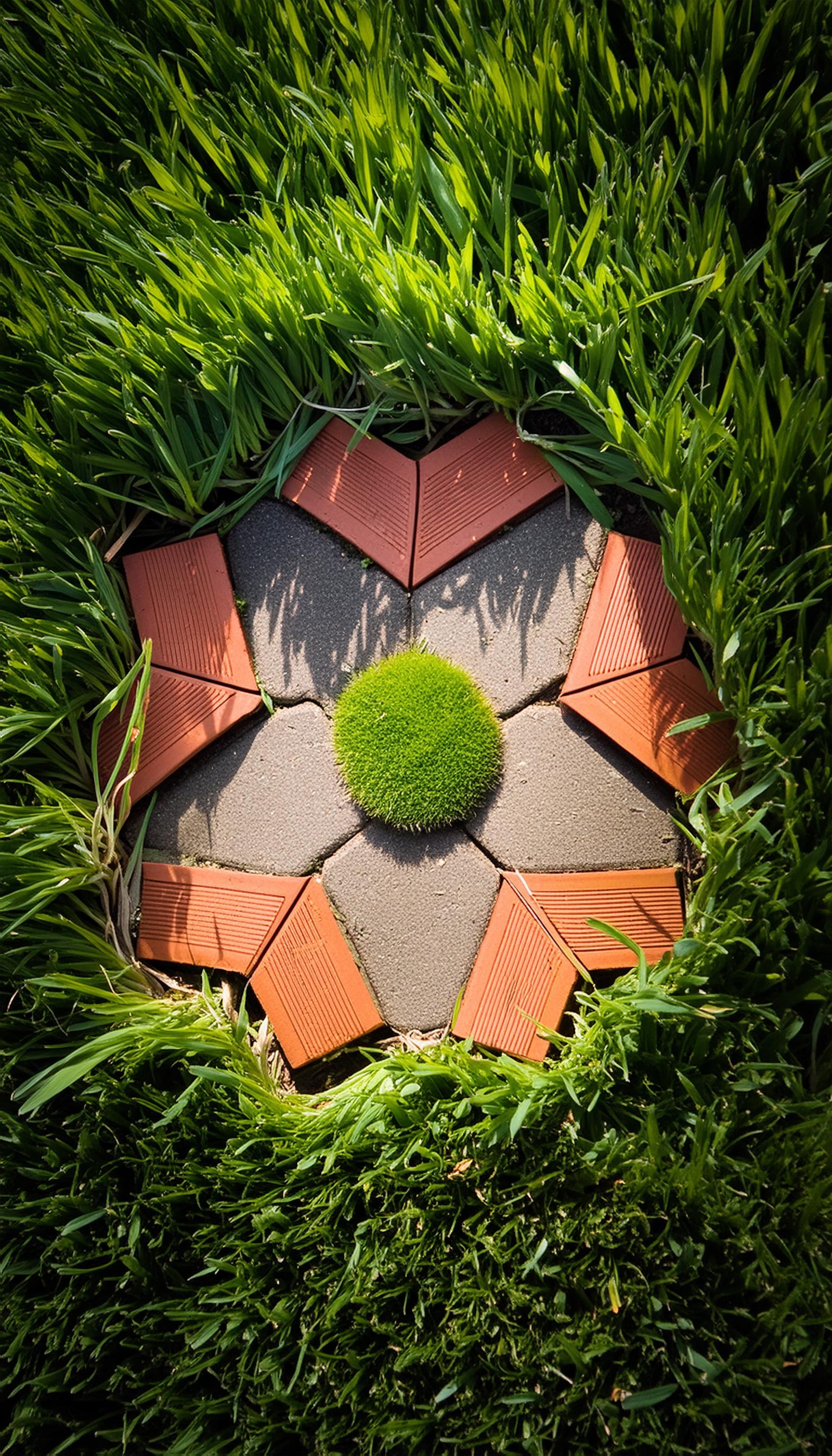 Artistic arrangement of paving bricks forming a star-like pattern resembling the Outli.ne logo, surrounded by lush green grass.