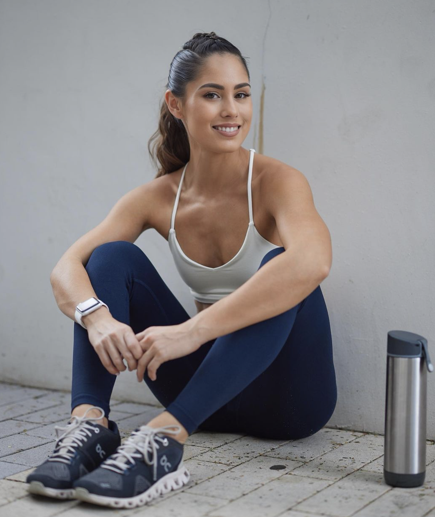 Valerie Senior seated on the ground in workout attire, smiling, with a water bottle nearby, exuding a casual and relaxed vibe post-exercise.