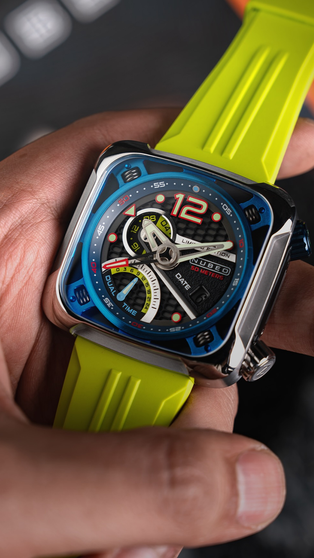 Close-up of a brightly colored wristwatch with a green strap, held by a hand; the watch face has various dials and details in red, blue, and yellow.