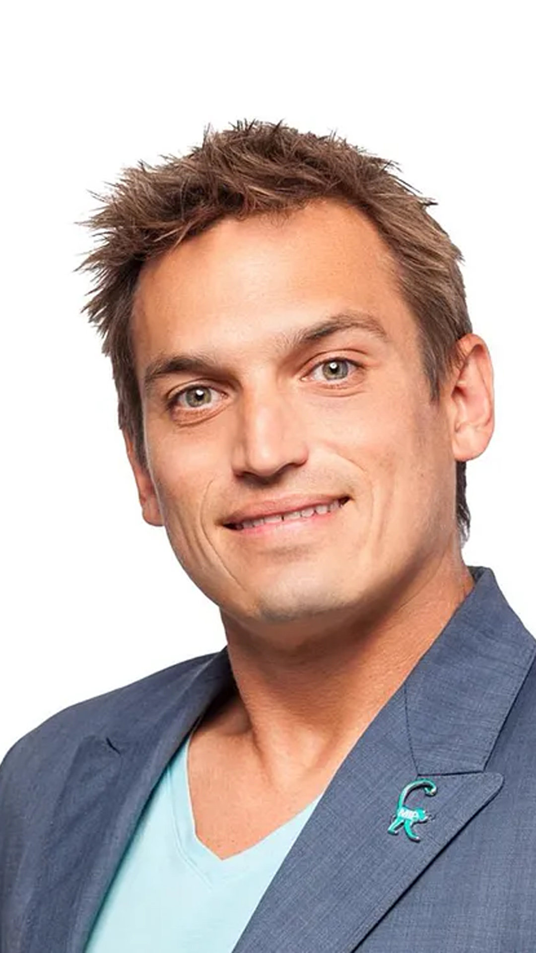 Smiling headshot of Alex Kowtun, with short, tousled hair, wearing a blue blazer over a turquoise shirt, set against a plain white background.