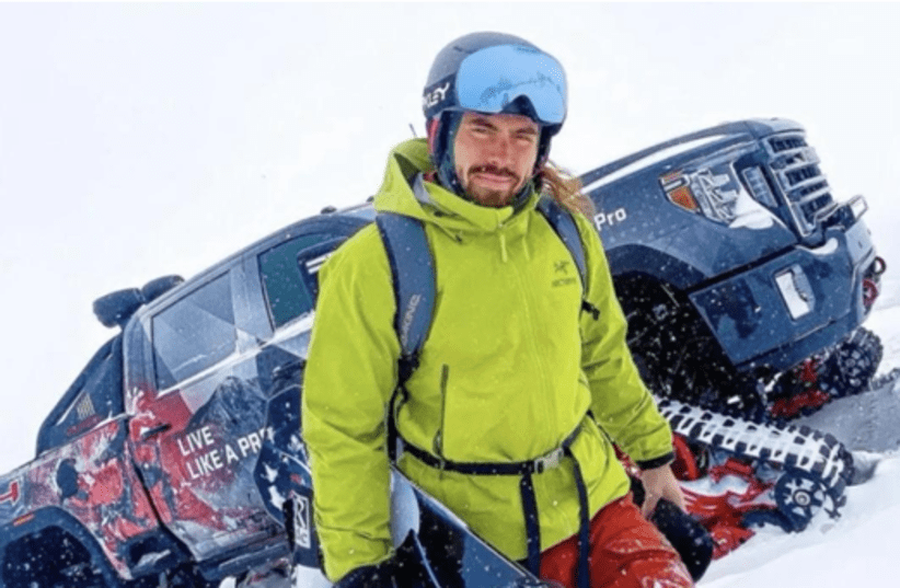 Tristan Hamm in a green jacket with a snowboard, standing in deep snow beside a modified truck decorated with 'Live Like a Pro' graphics.