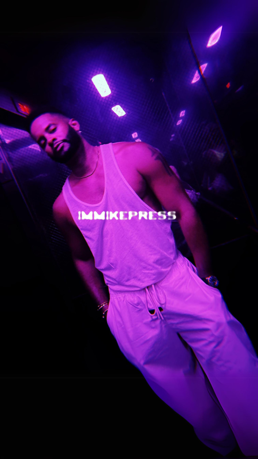 Mike Press leaning against a purple-lit wall wearing a white tank top and sweatpants with 'IMMKEPRESS' text overlayed; the ambiance is dim with neon accents.