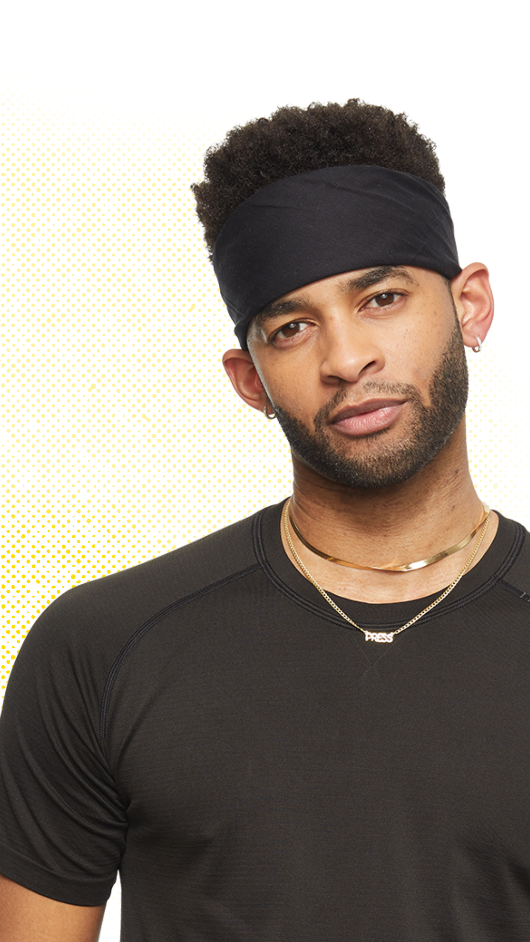 Mike Press with curly hair wearing a black headband, gold necklace, and black T-shirt, looking at the camera against a dotted background.