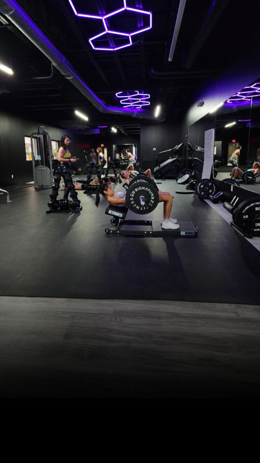 Another angle of the gym featuring weightlifting equipment and people engaged in workout activities.